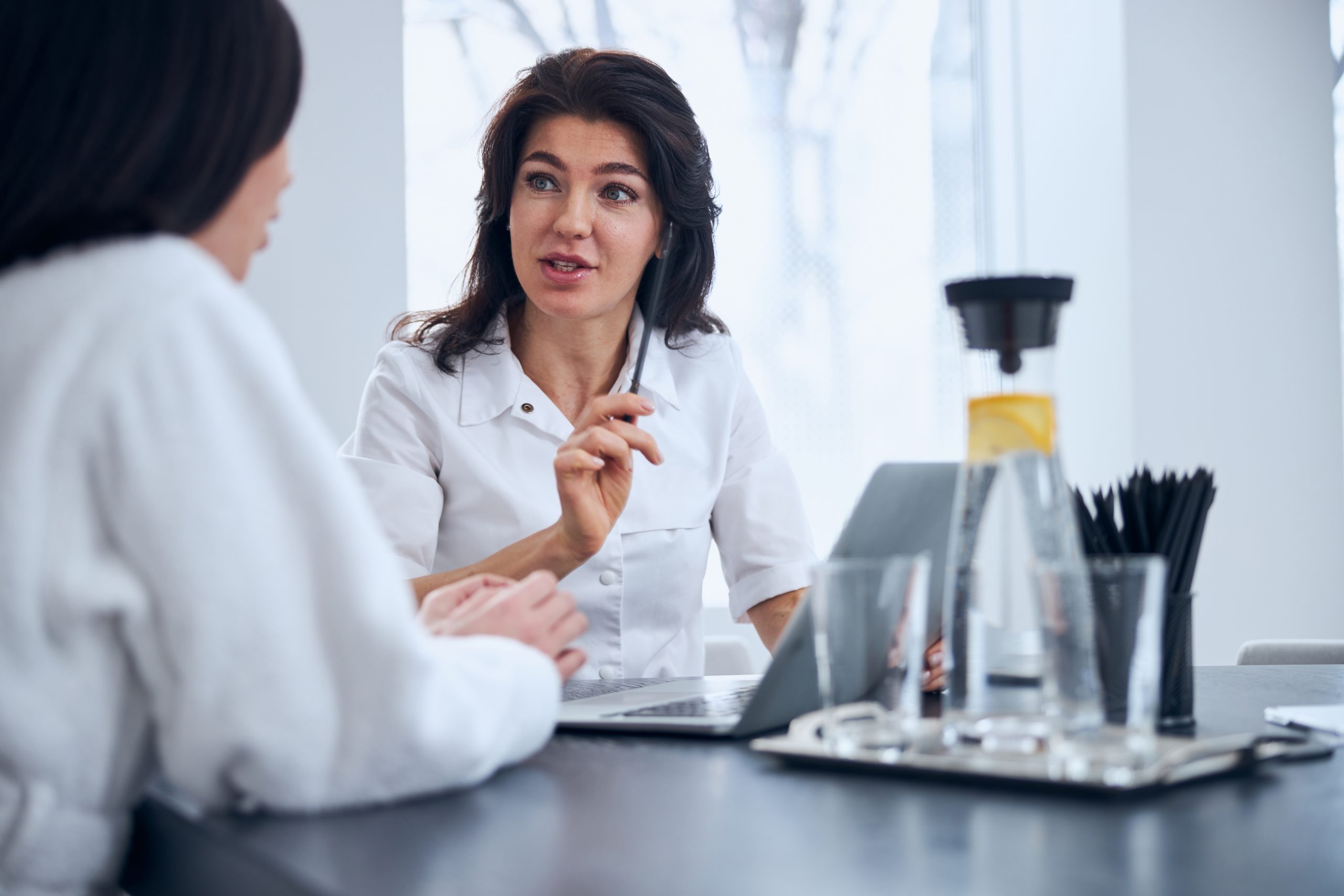 Middle-aged physician with a pen in her hand staring at a dark-haired woman during the consultation